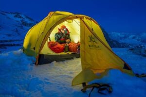 Vuorikiipeilijä istuu valaistussa teltassa lumisessa vuoristossa